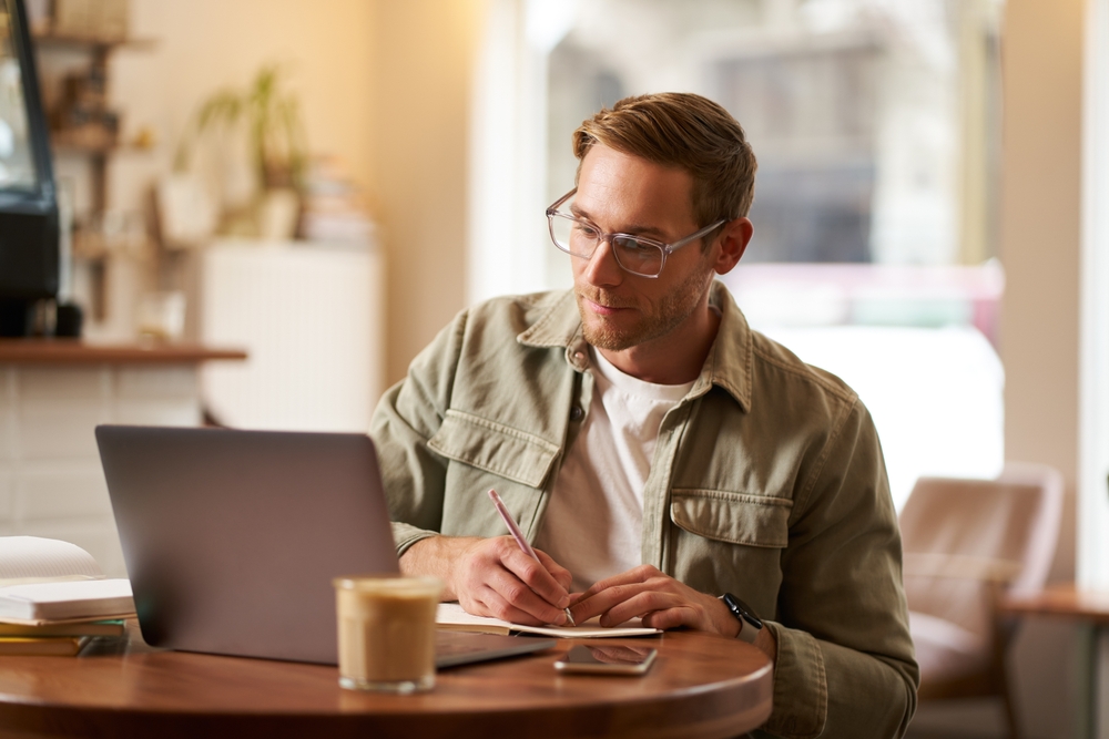 Man Focussing At Laptop Making Notes